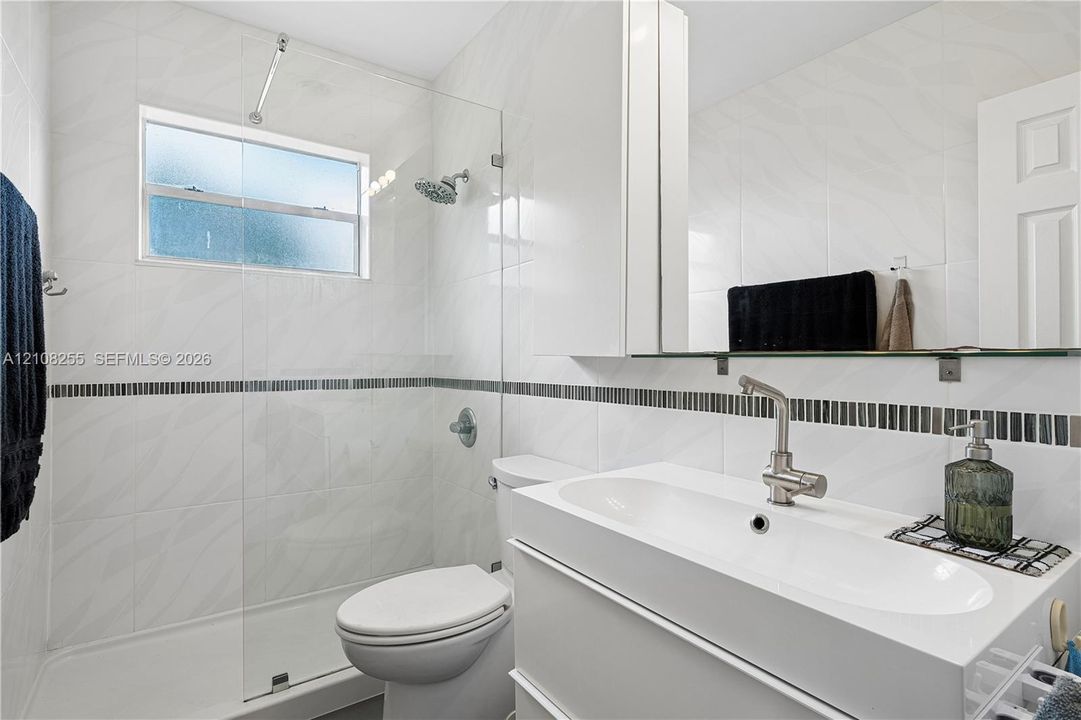 Bathroom featuring white wall tile with a mosaic accent border, a glass-enclosed shower, a floating vanity with an integrated sink, and brushed-nickel hardware
