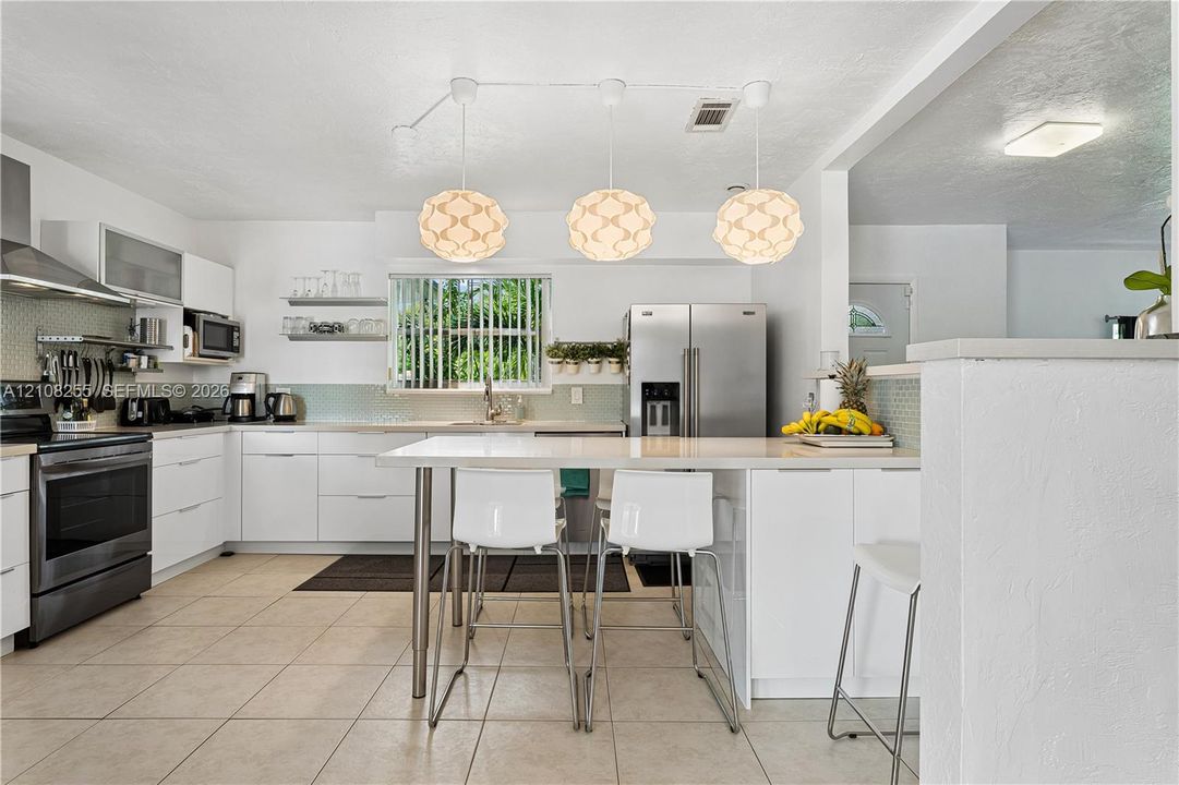 Kitchen featuring flat-panel white cabinetry, stainless steel appliances, quartz countertops, a tile backsplash, and three suspended geometric pendant lights