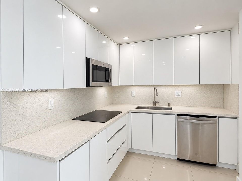 Kitchen featuring flat-panel white cabinetry, stone-surface countertops, integrated stainless steel appliances, recessed lighting, and large-format tile flooring
