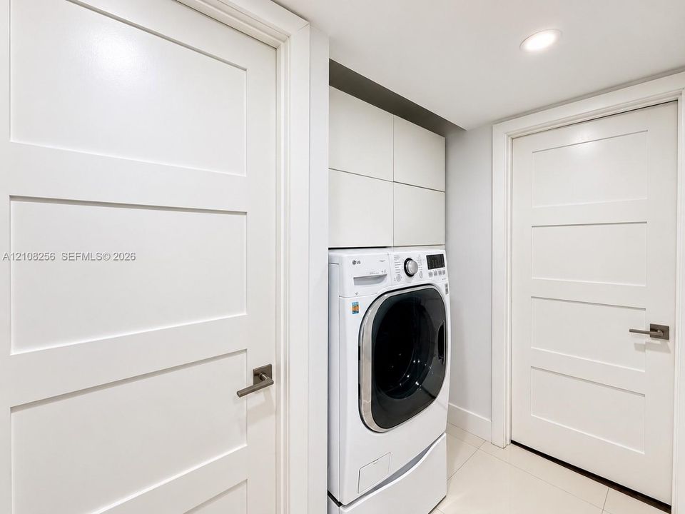 Laundry area featuring built-in cabinetry, recessed lighting, and tile flooring, framed by two white Shaker-style doors with metallic lever handles