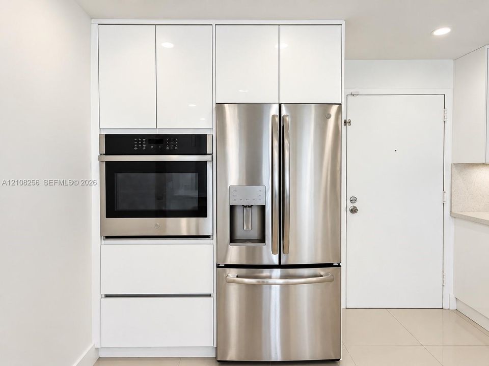 Kitchen featuring floor-to-ceiling high-gloss white cabinetry, integrated stainless steel wall oven, and French-door stainless steel refrigerator