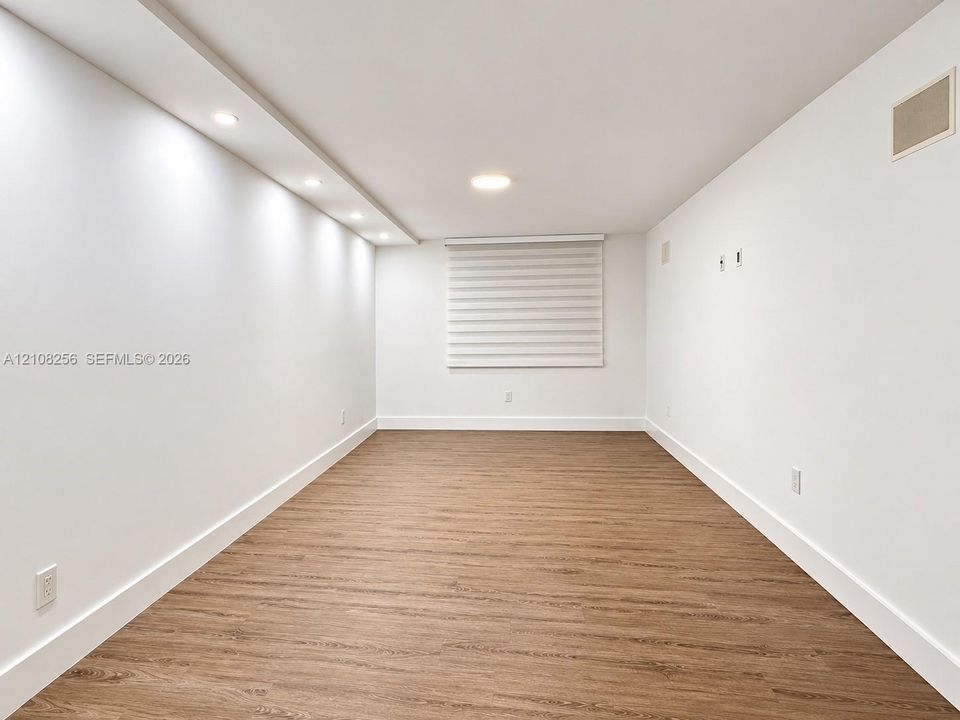 Wood-finish flooring, recessed lighting, integrated ceiling cove lighting, and window with white roller shade