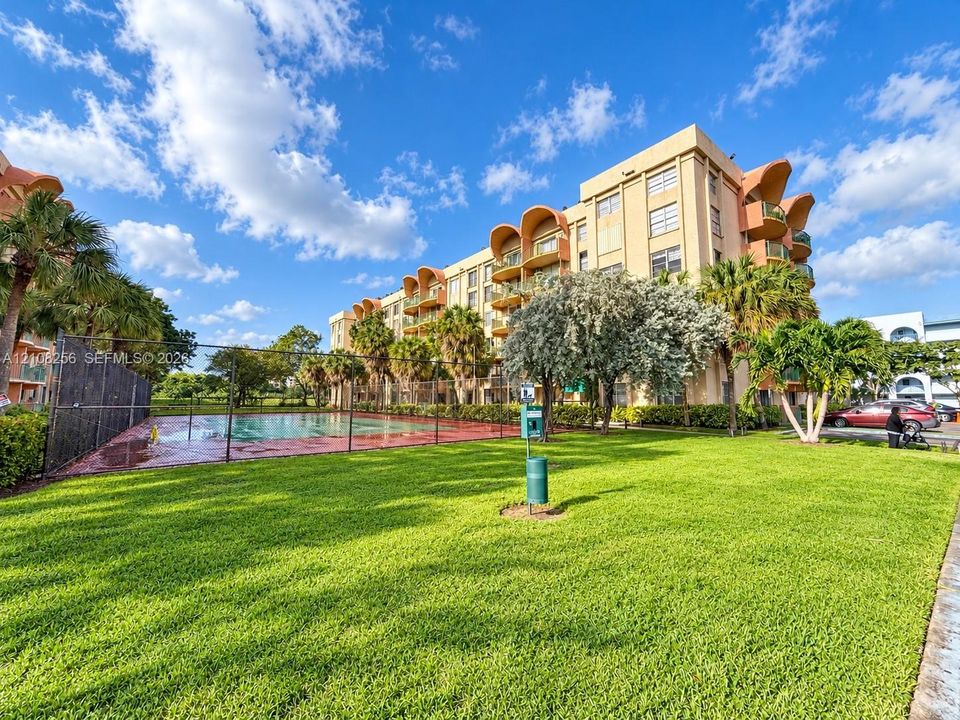 Multi-story building featuring architectural arched balconies, fenced swimming pool, and landscaped green space with mature palm trees