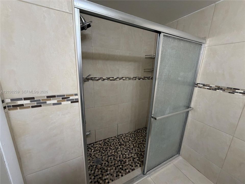Walk-in shower featuring large-format wall tile, a multi-colored stone mosaic accent band, a pebble-finish floor, and a sliding glass door enclosure