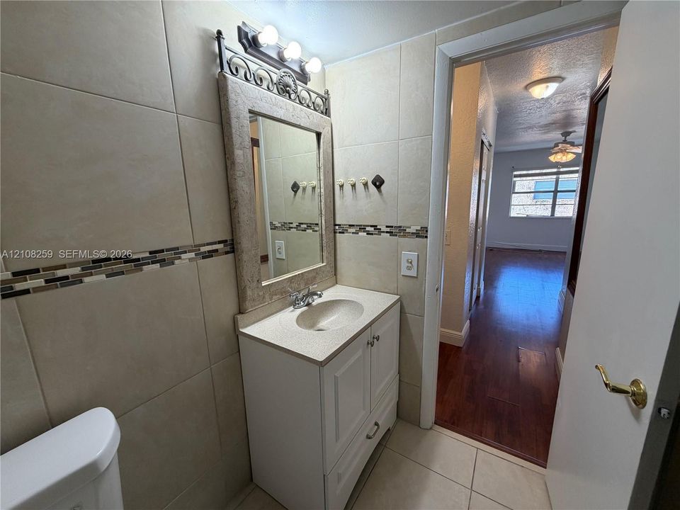 Bathroom featuring tile wall cladding with a decorative mosaic accent border, a white vanity with an integrated sink, a framed vanity mirror, and three-bulb vanity lighting