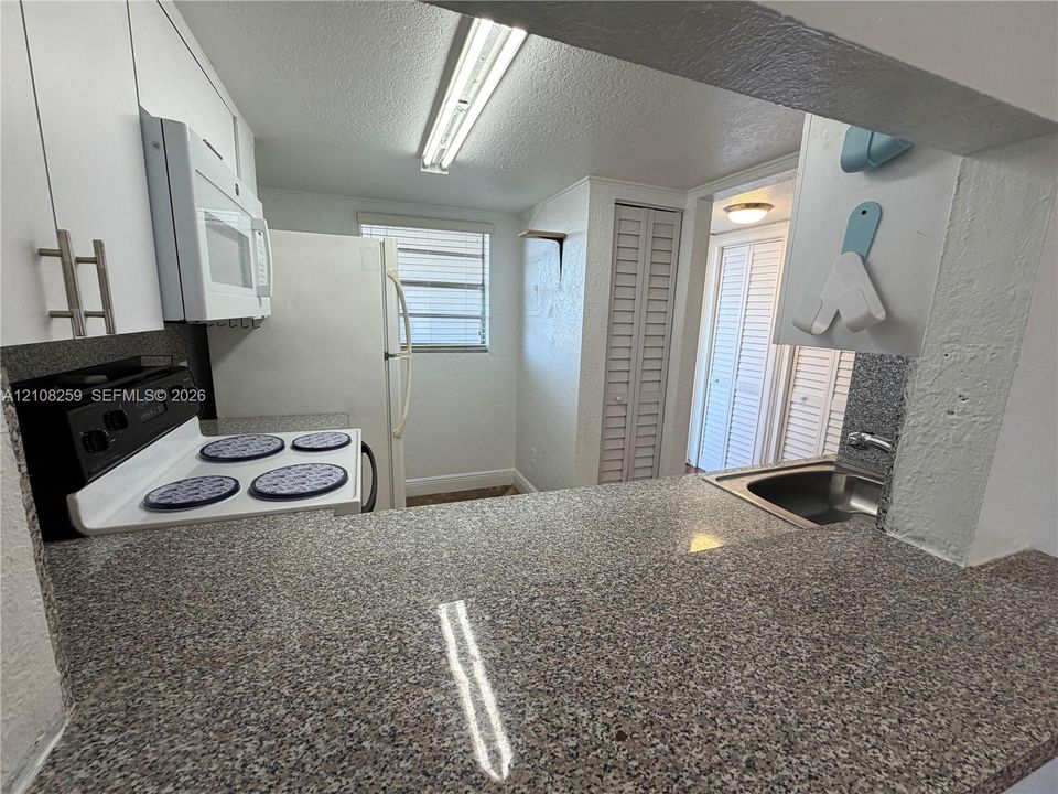 Kitchen featuring stone-finish countertops, white cabinetry with metallic hardware, and white appliances