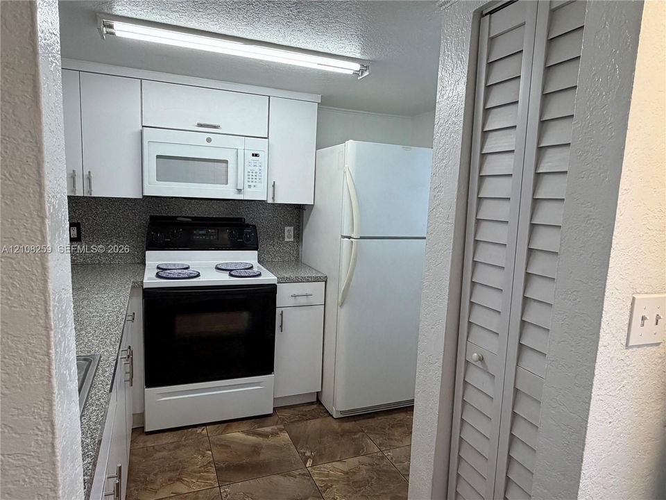 Kitchen featuring white cabinetry, speckled stone-finish countertops, built-in microwave, integrated refrigerator, and tile flooring