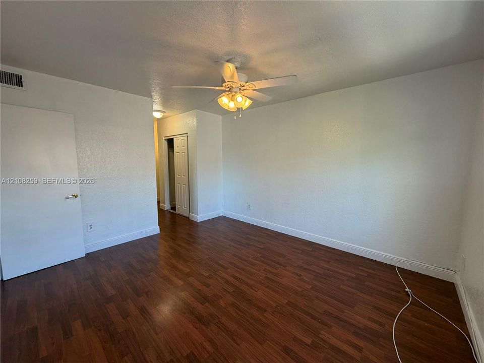 Room featuring dark wood-finish flooring, white walls, and a ceiling-mounted light fixture with a fan