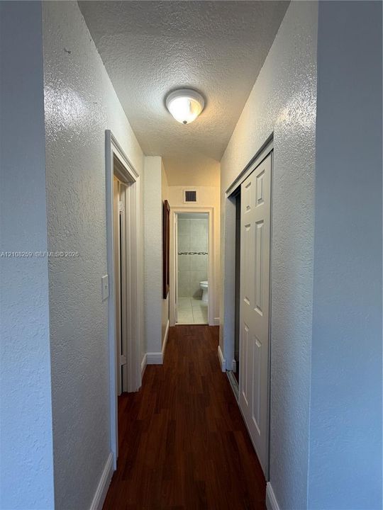 Hallway featuring wood-finish flooring, white walls, and a ceiling-mounted light fixture, with a bifold closet door and a passage leading to a tiled room