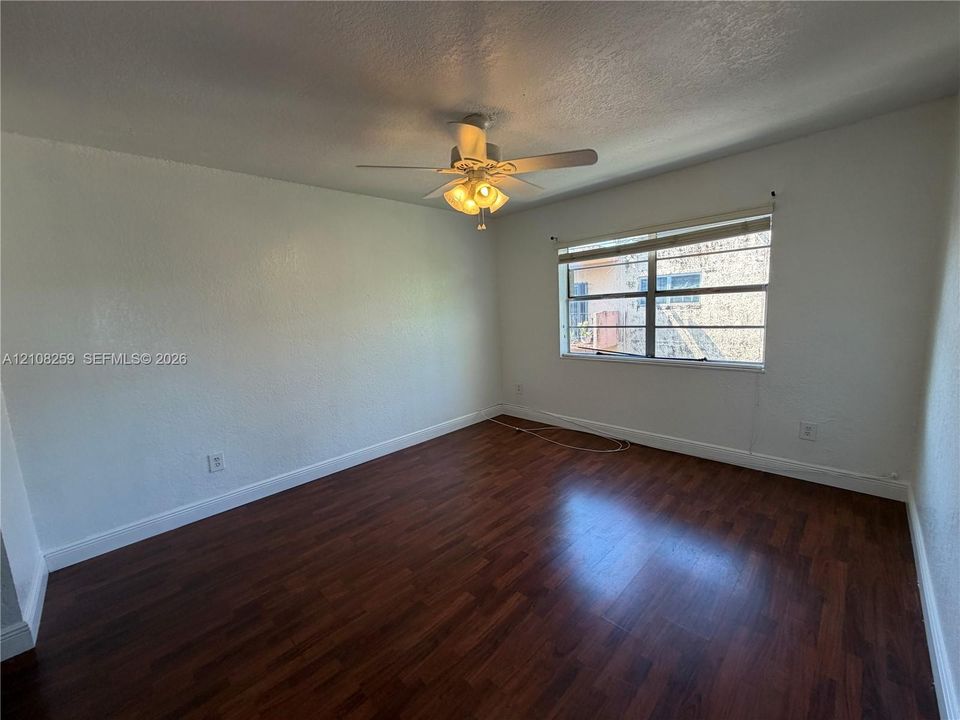 Room featuring dark wood-finish flooring, a multi-blade ceiling fan with integrated light fixture, and large window with horizontal blinds