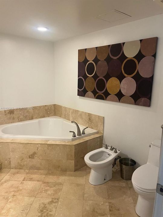Corner soaking tub with natural stone surround, stone tile flooring, bidet, and two-piece toilet