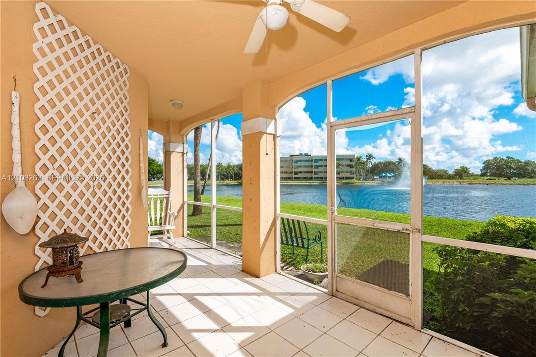 Screened-in lanai featuring white ceramic tile flooring, a mounted ceiling fan, decorative wall-mounted latticework, and water frontage