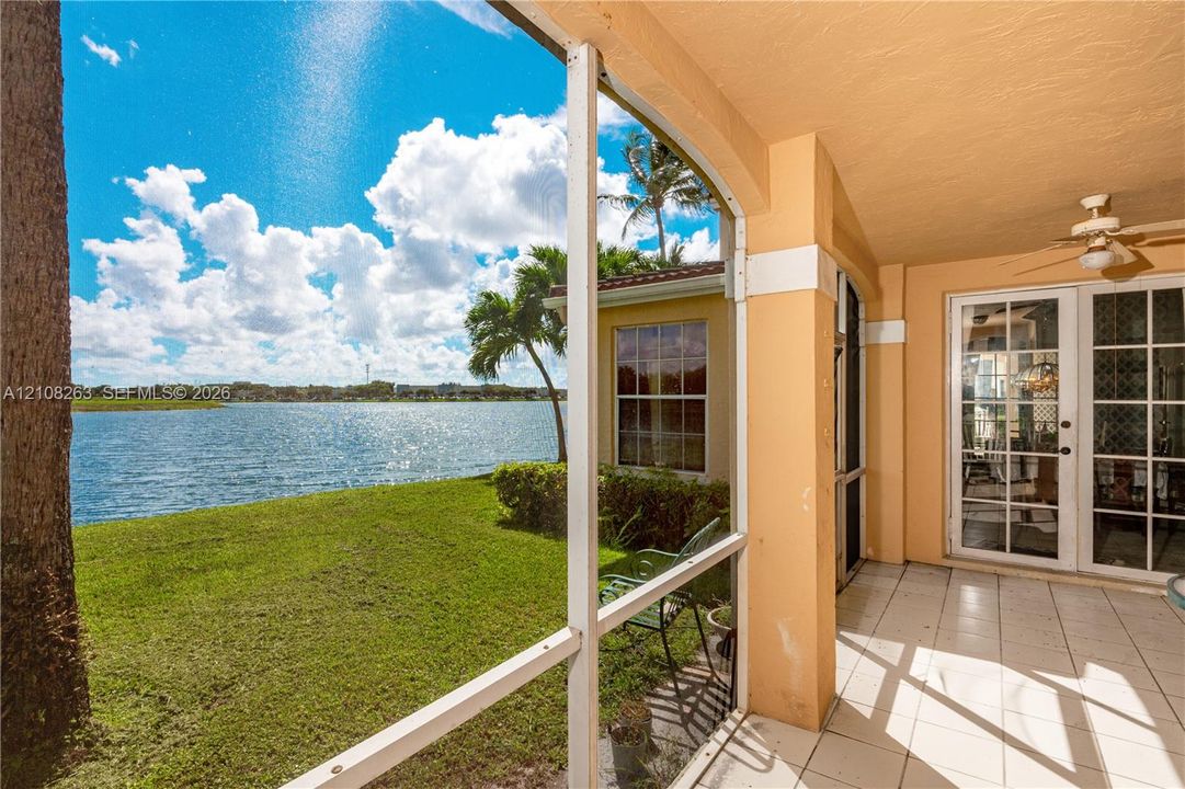 Covered screened-in patio featuring tile flooring, a ceiling fan, and sliding glass door access, overlooking a waterfront lawn