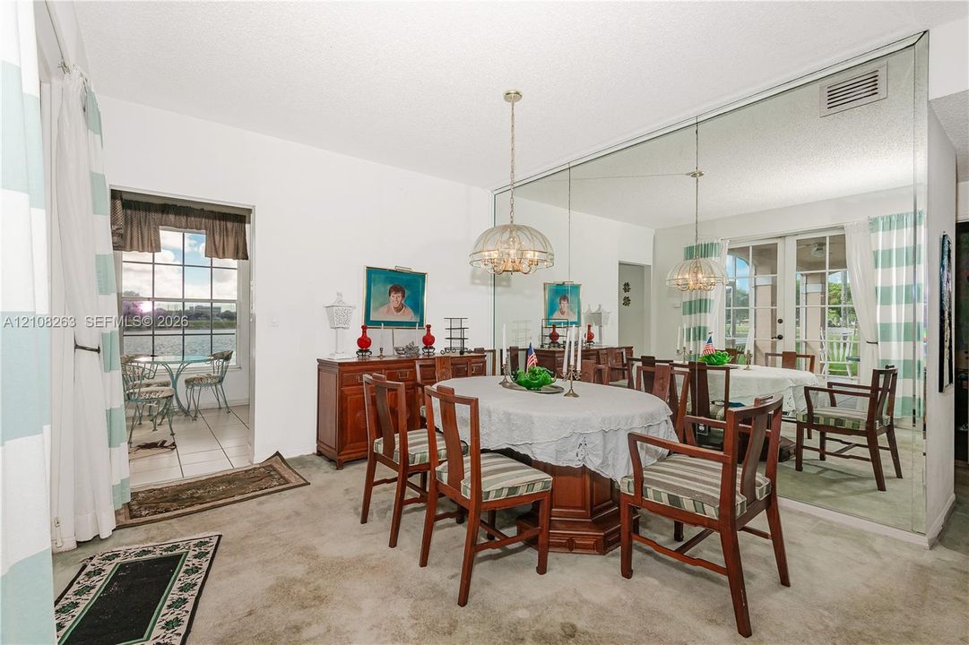 Dining space featuring a floor-to-ceiling wall mirror, a central pendant light fixture, and an entry to an exterior-facing patio