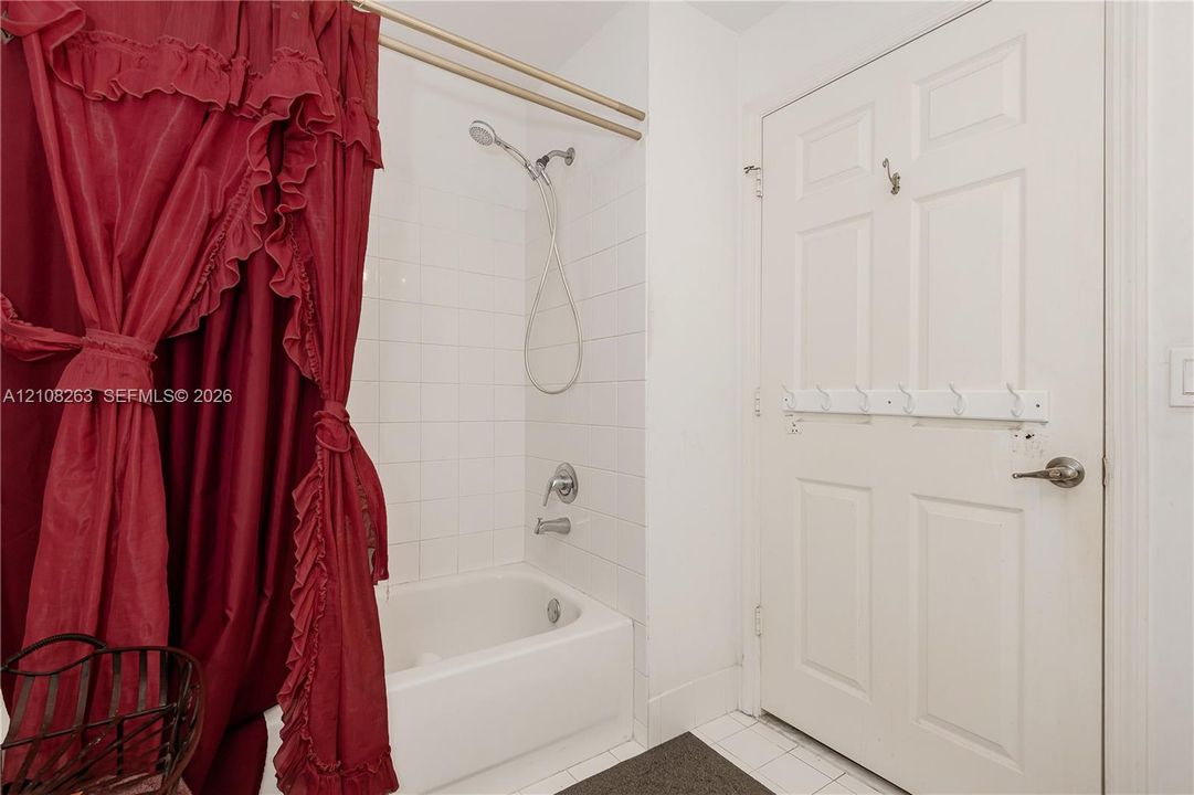 Bathroom featuring a white composite bathtub, wall-mounted shower head, tiled surround, and a six-panel door with integrated hardware