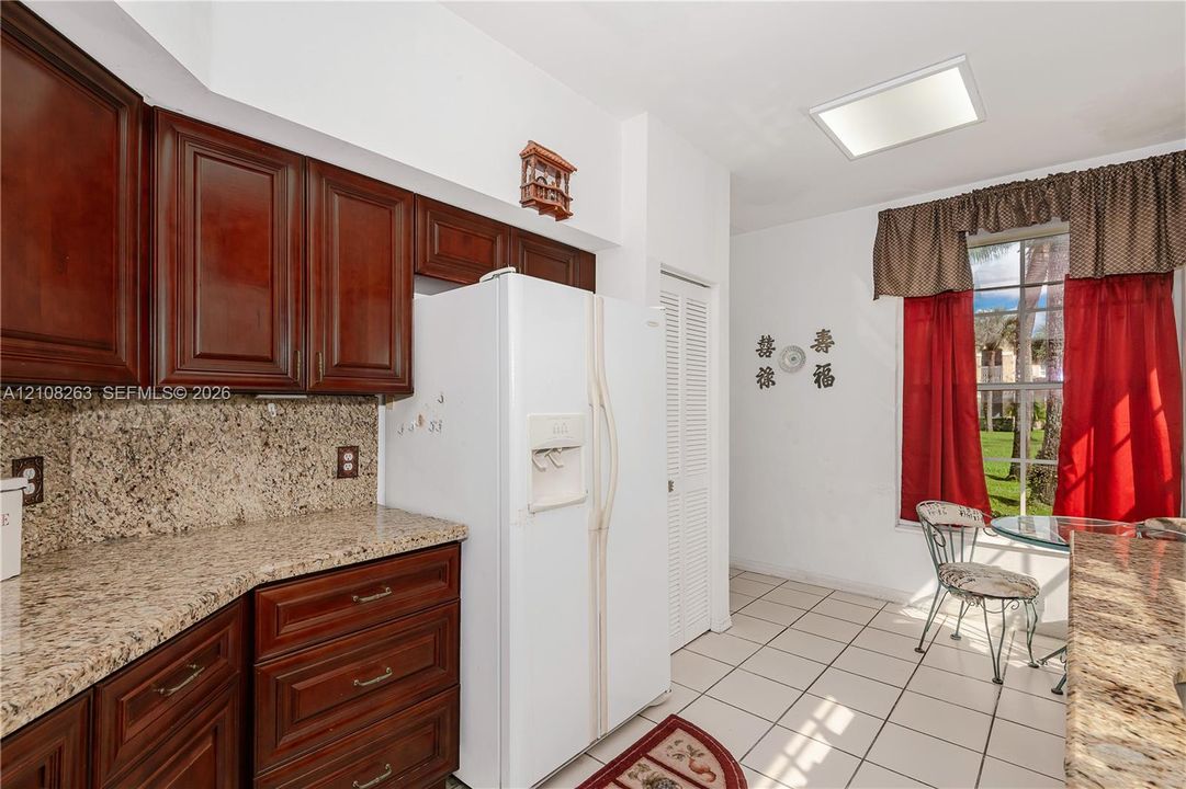 Kitchen featuring dark-stained wood cabinetry, stone countertops, tiled flooring, a skylight, and a large window