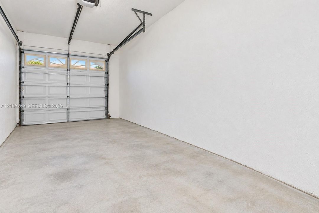 Enclosed garage featuring finished white walls, a concrete floor, and an overhead sectional door with integrated glazing panels