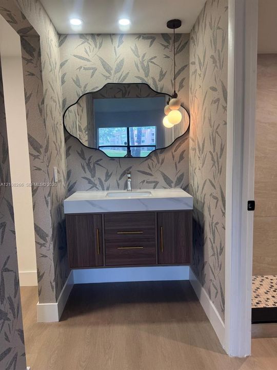 Floating wood-finish vanity with a rectangular sink, quartz countertop, custom-shaped wall mirror, and modern pendant lighting