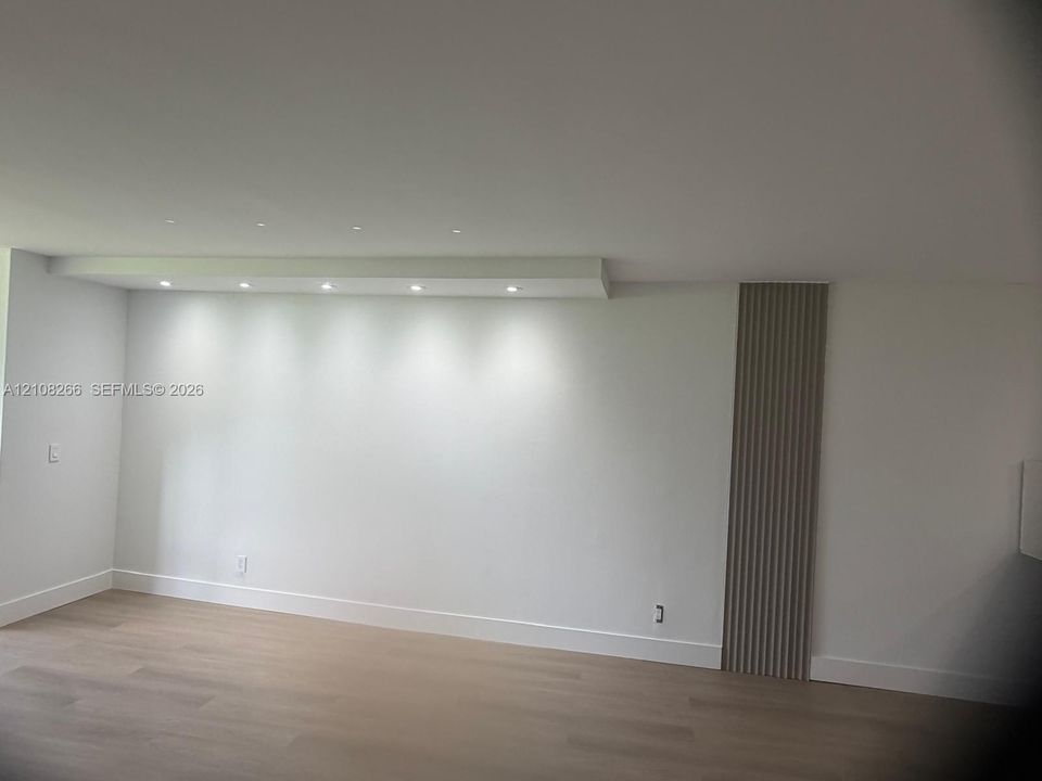 Minimalist interior featuring recessed ceiling lighting, light-toned wood-finish flooring, and a decorative vertical slat accent wall