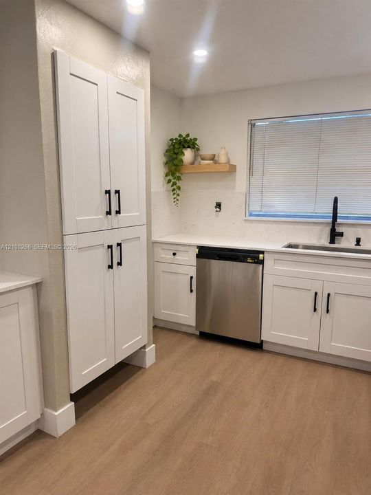 White Shaker-style cabinetry featuring matte black hardware, stone-finish countertops, stainless steel dishwasher, undermount sink with a matte black faucet, and wood-finish flooring