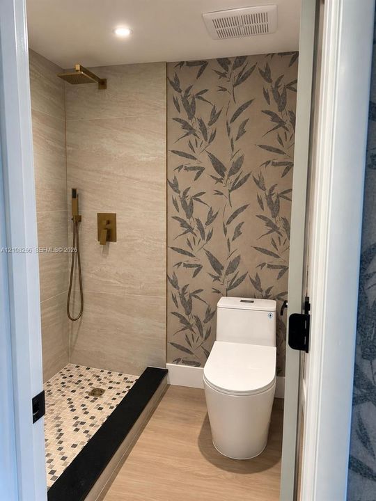 Walk-in shower with stone-finish tile surround, gold-tone hardware, multi-colored mosaic tile flooring, and contrasting black threshold
