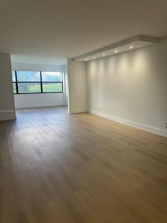 Open-concept interior featuring light wood-finish flooring, a recessed soffit with integrated downlighting, and large-format multi-pane windows