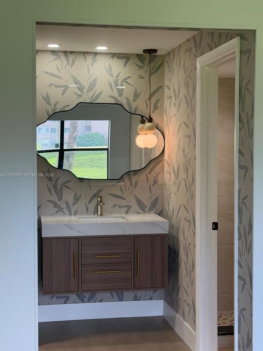 Floating wood-finish vanity with a quartz countertop, integrated basin, brushed brass hardware, scalloped-edge wall mirror, and dual-globe pendant lighting
