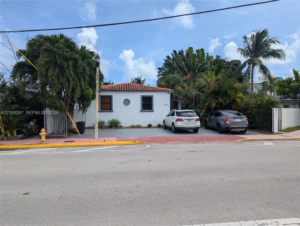 Stucco exterior featuring a terracotta-tiled hip roof, multi-car paved parking area, and mature tropical landscaping
