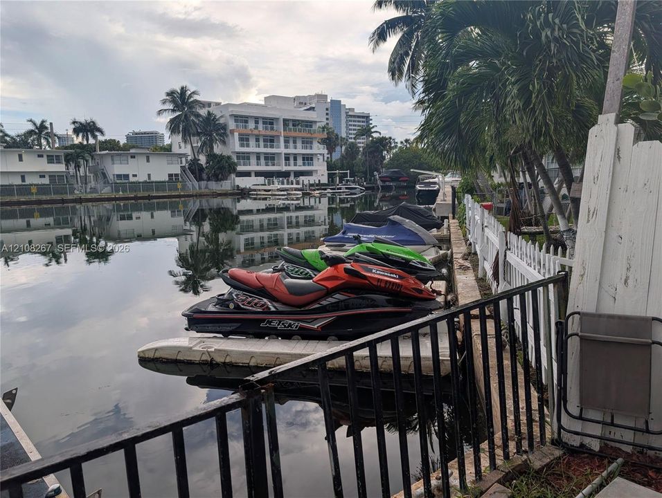 Waterfront property featuring a canal-side floating dock, black metal perimeter fencing, and mature palm trees