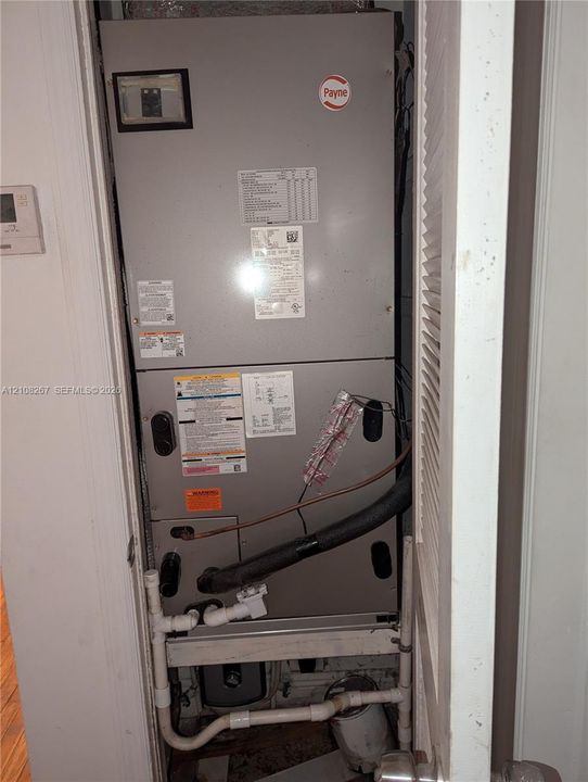 Payne furnace unit featuring a metal enclosure with built-in plumbing connections and a mounted digital thermostat