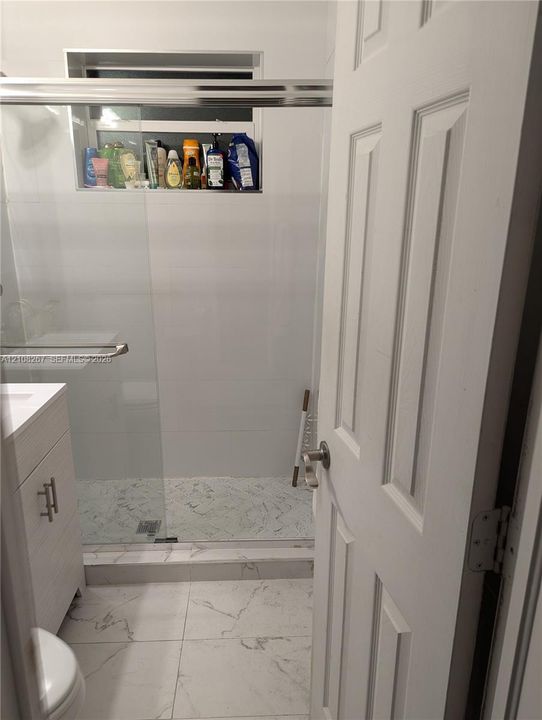 Bathroom featuring a walk-in shower with a glass enclosure, built-in tiled niche, stone-patterned floor tiling, and a vanity with a white cabinet