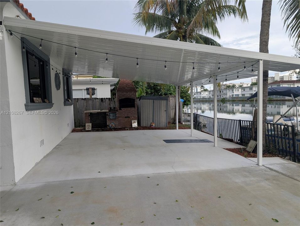 Covered patio featuring a concrete slab, built-in brick fireplace, and metal roof structure overlooking a canal