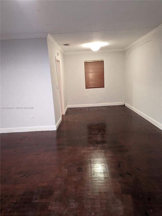 Interior space featuring dark wood-finish flooring, crown molding, and a single window with slatted blinds