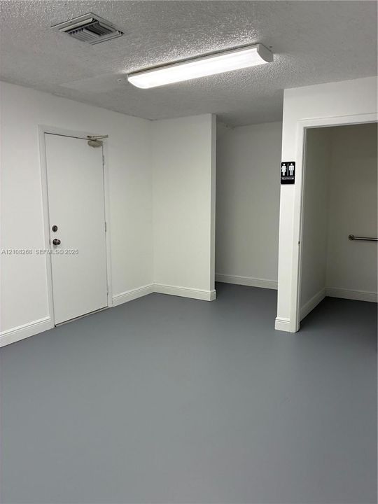 Neutral-toned interior space featuring solid-surface flooring, flush-mount lighting, and a metal-clad entry door