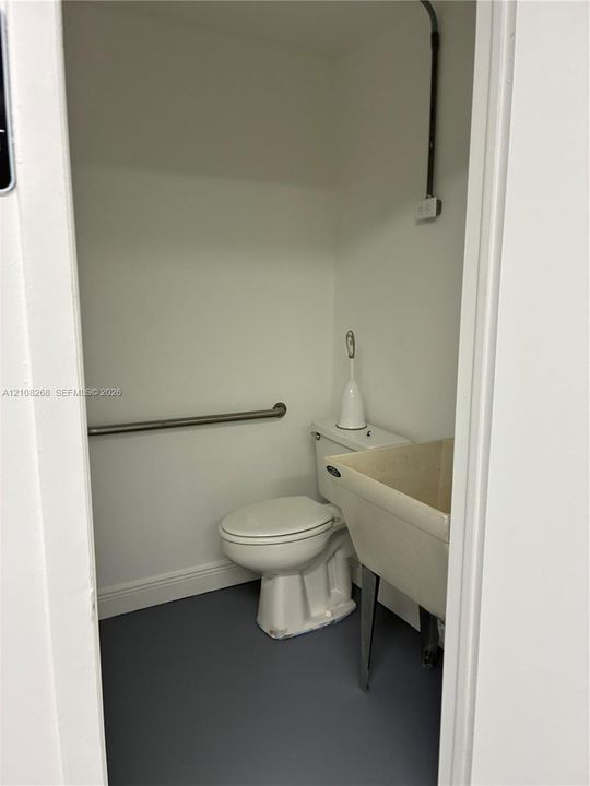 Restroom featuring an integrated utility sink, two-piece toilet, stainless steel grab bar, and resilient dark-tone flooring