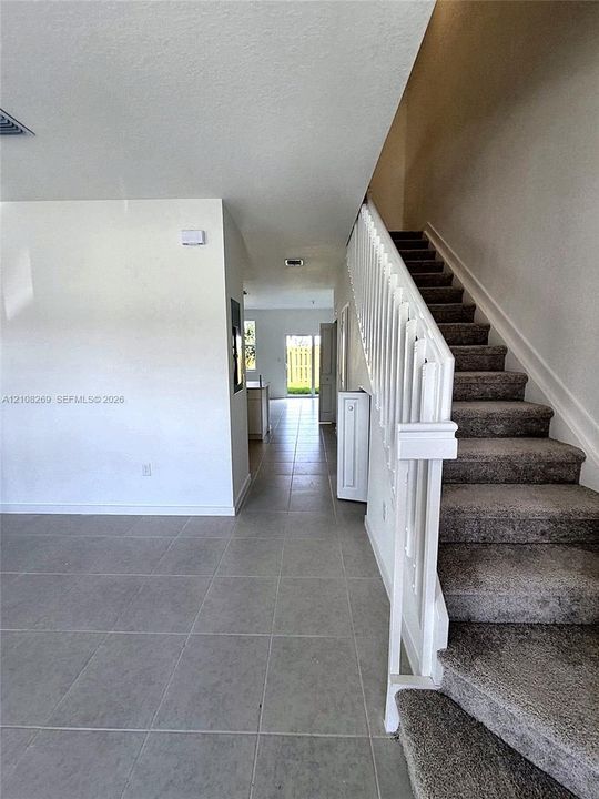 Large-format tile flooring, staircase with white railing, and neutral wall finish