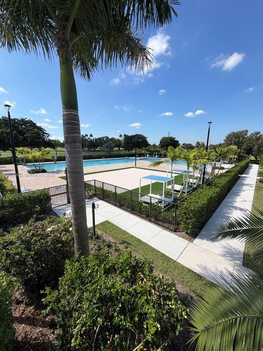 Swimming pool with concrete decking, surrounding black metal fencing, synthetic turf accents, and perimeter landscaping