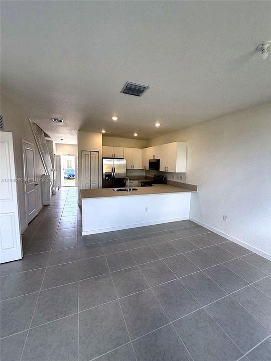 Kitchen featuring white cabinetry, solid-surface countertops, stainless steel appliances, and large-format tile flooring