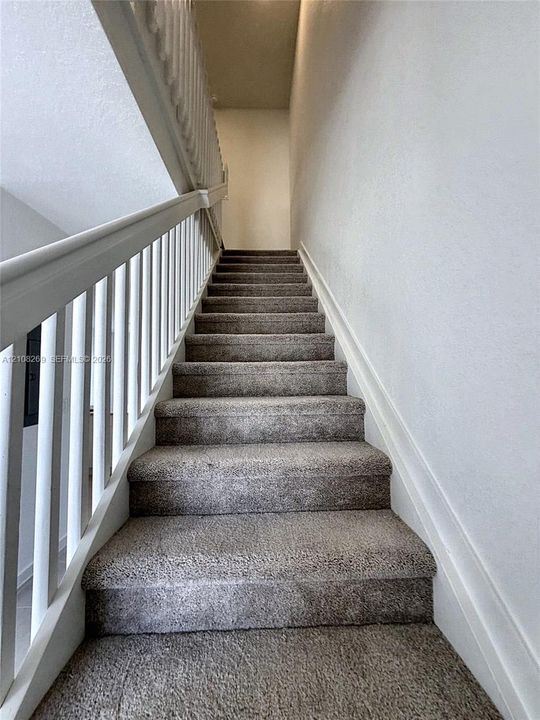 Staircase featuring wall-to-wall carpeting, white wooden balusters, and a matching handrail