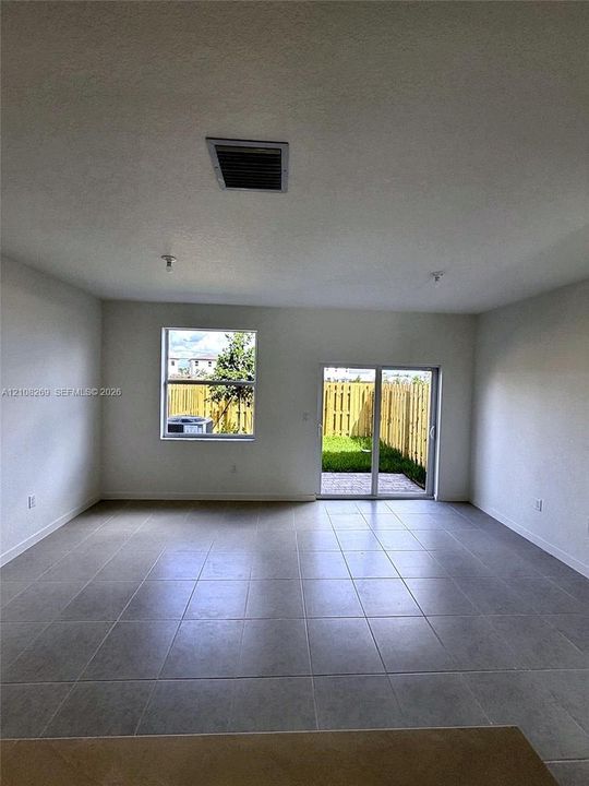 Open-concept interior featuring large-format ceramic tile flooring, neutral walls, a single-hung window, and a sliding glass door providing external access