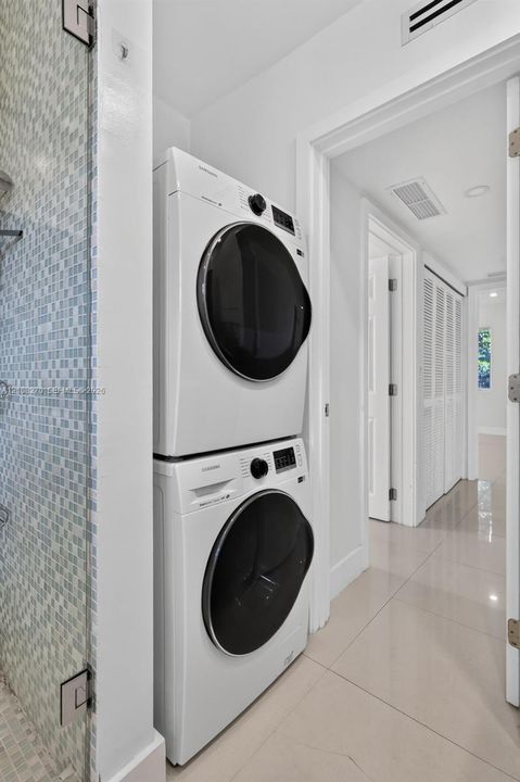 Laundry area featuring a stacked washer and dryer unit, glass-enclosed shower with mosaic wall tile, and large-format tile flooring