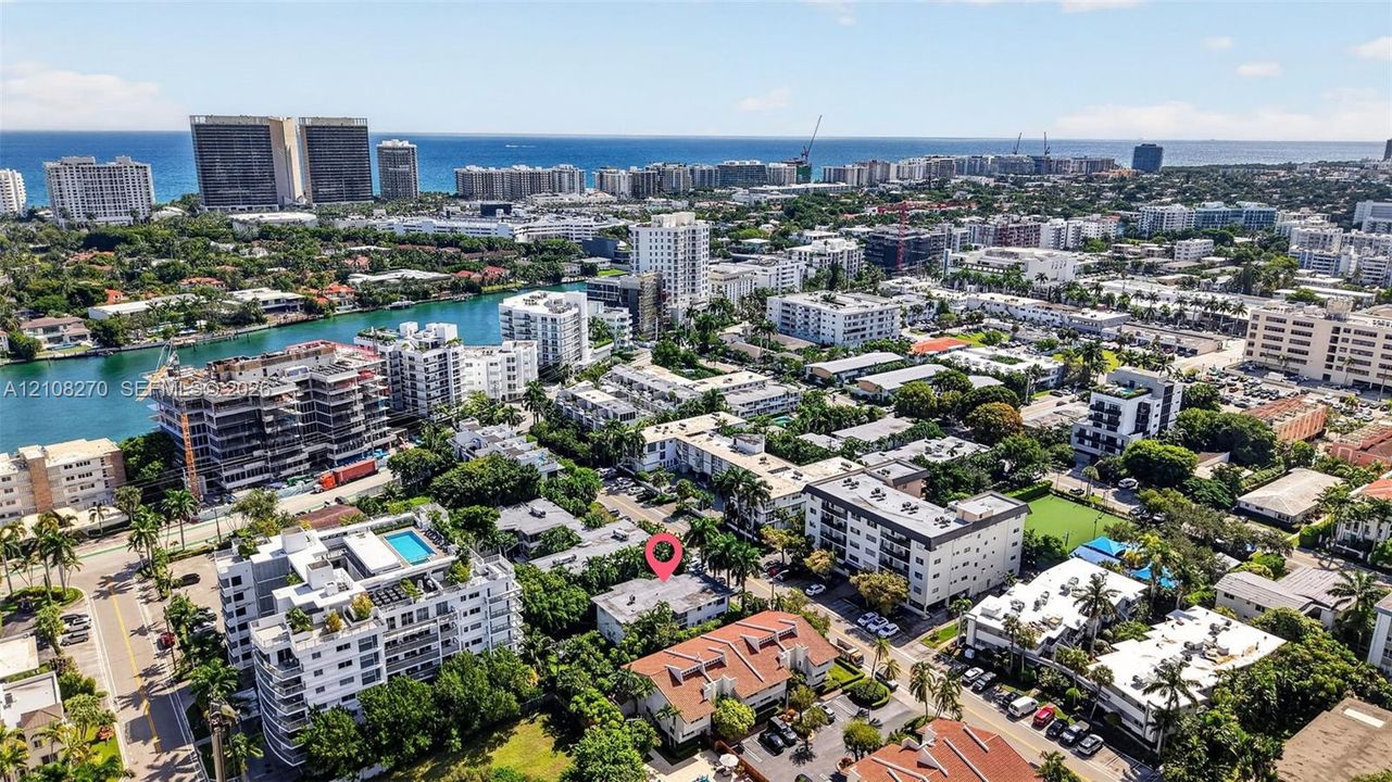 Aerial perspective of a multi-story residential building featuring a flat roofline, integrated parking area, mature landscaping, and positioning within a coastal urban setting