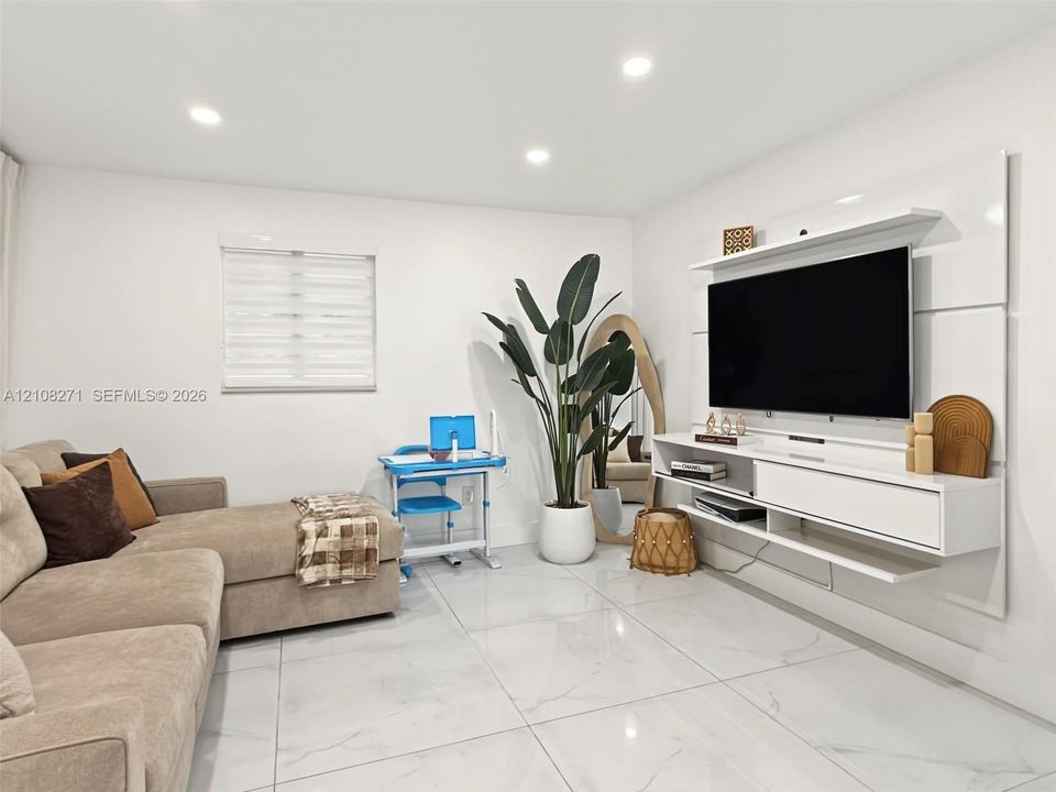 Large-format porcelain tile flooring with a light marbled finish, complemented by a white wall-mounted media console and recessed ceiling lighting