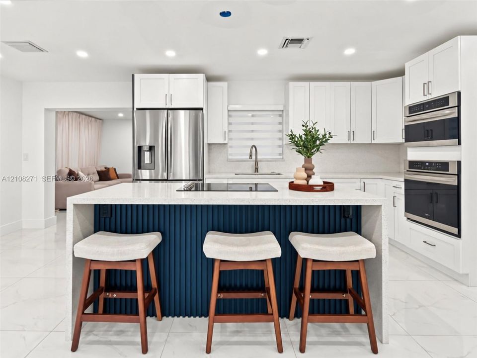 Kitchen featuring a central island with a fluted navy base and stone countertop, white cabinetry, built-in stainless steel double ovens, and large-format tile flooring
