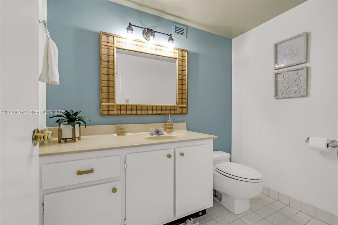 Bathroom featuring a white vanity cabinet with an integrated sink, neutral countertop, wall-mounted light fixture, and tile flooring