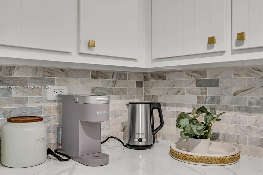 Kitchen featuring white shaker-style cabinetry, gold-tone hardware, and a natural stone tile backsplash