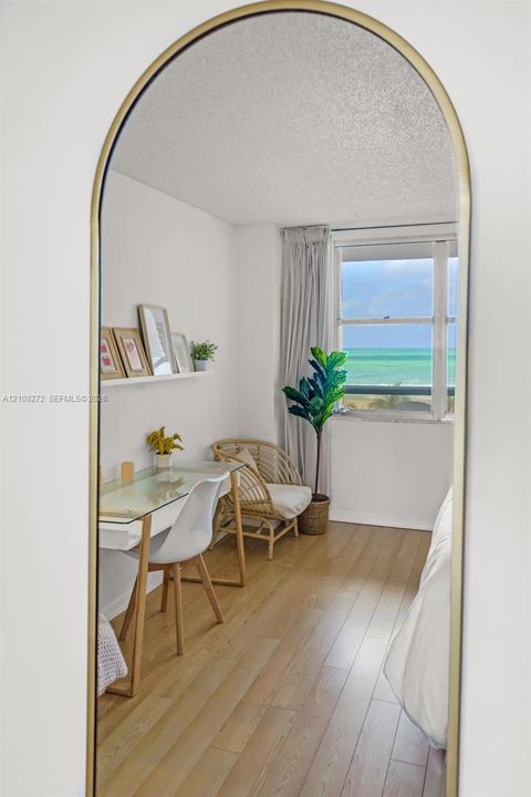 Arched wall mirror with a gold-tone frame, wood-finish flooring, and large window with ocean scenery