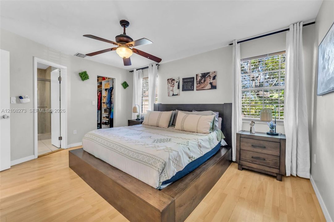 Bedroom featuring light wood-finish flooring, a ceiling fan with integrated lighting, and a walk-in closet with built-in organization