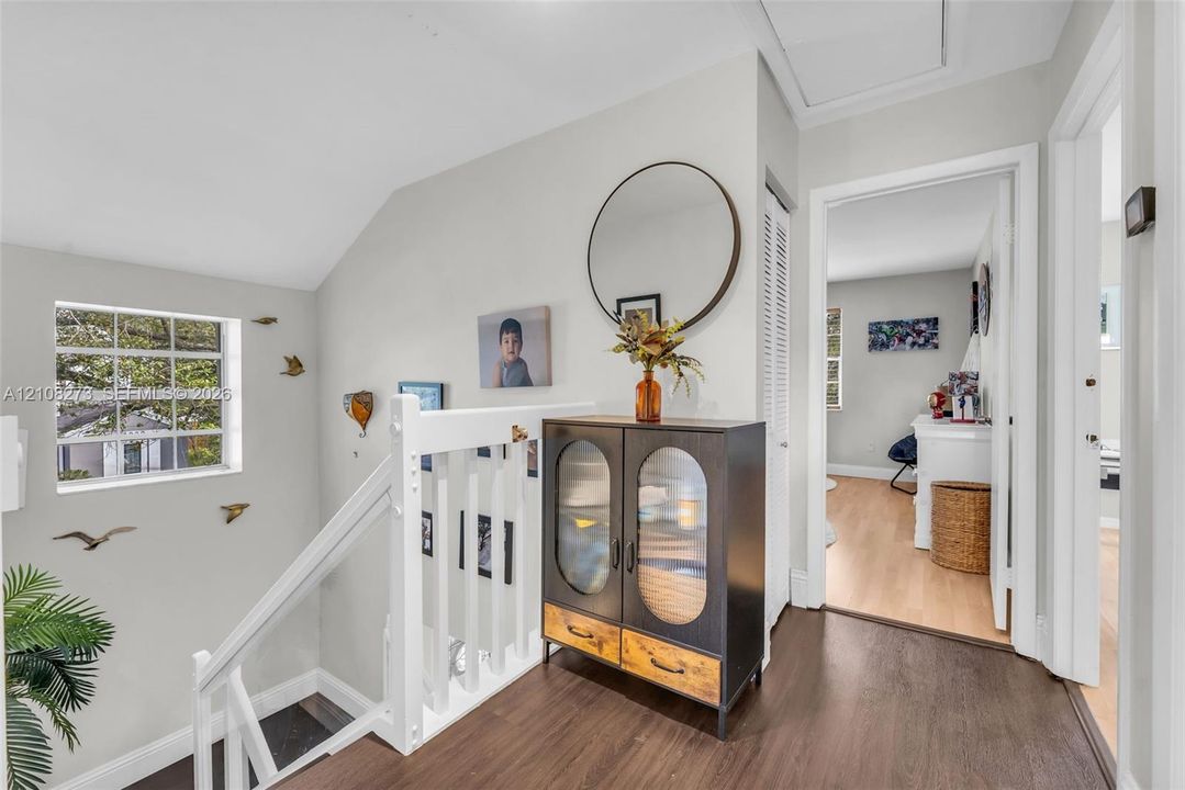 White wooden railing with balusters, wood-finish flooring, multi-pane window, and louvered closet door