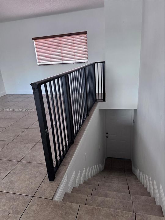Staircase featuring tile treads and a black metal handrail